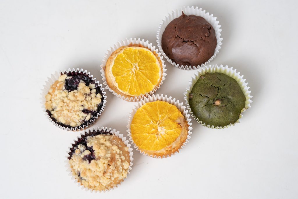 A delicious assortment of muffins featuring blueberry, chocolate, orange, and green tea flavors, beautifully arranged.