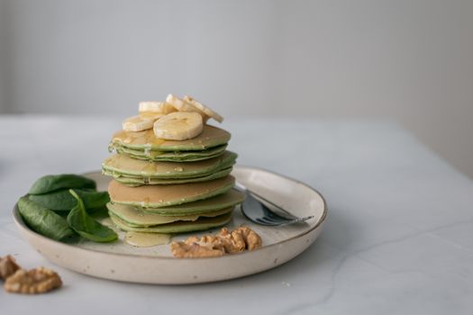 Portion of appetizing pancakes served on plate with fresh green leaves and knife with fork on white blurred background